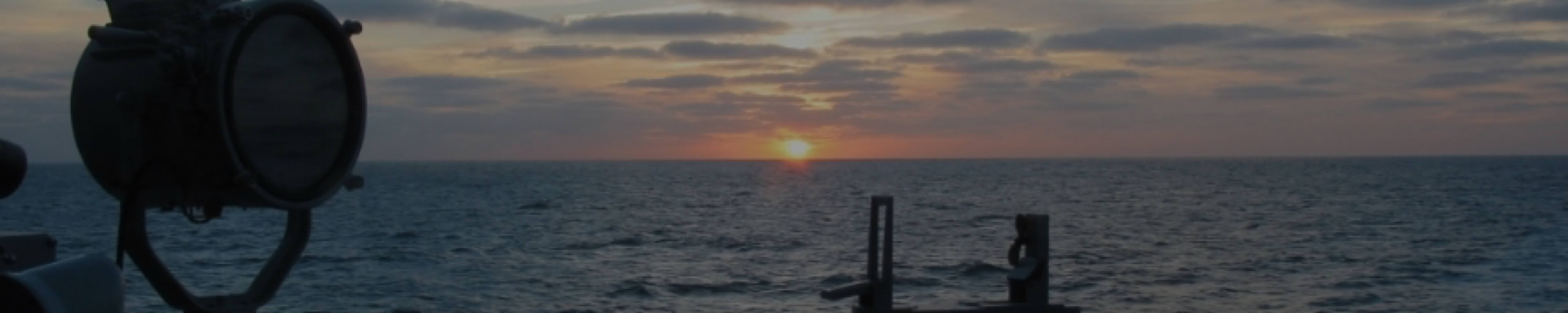 Zonsondergang op zee, gezien vanaf een M-Fregat met kompas en seinlamp op de voorgrond.